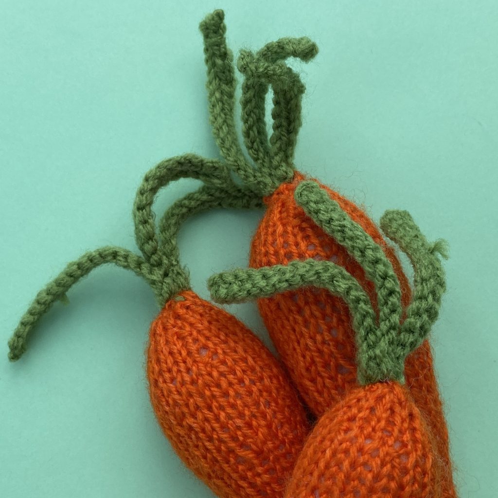 Knitted carrots from free carrot knitting pattern. Showing close up of top of carrots and green knitted stalks.