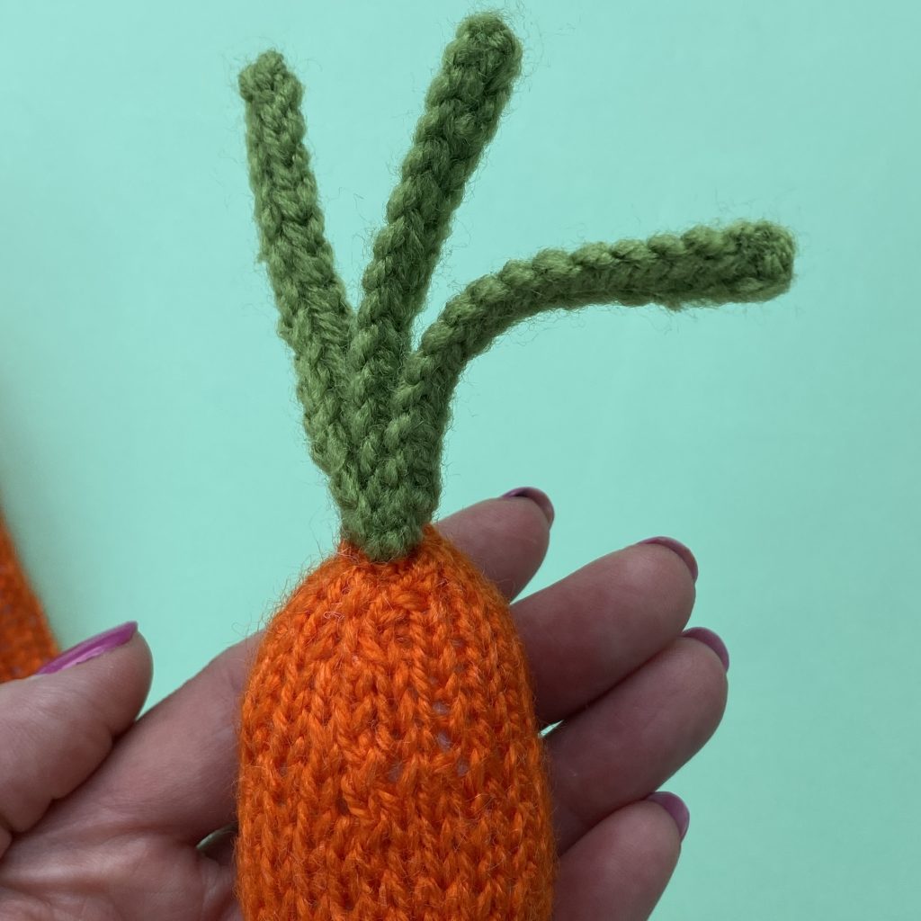 The stalks of a knitted carrot made from this free knitting pattern that is easy to follow 