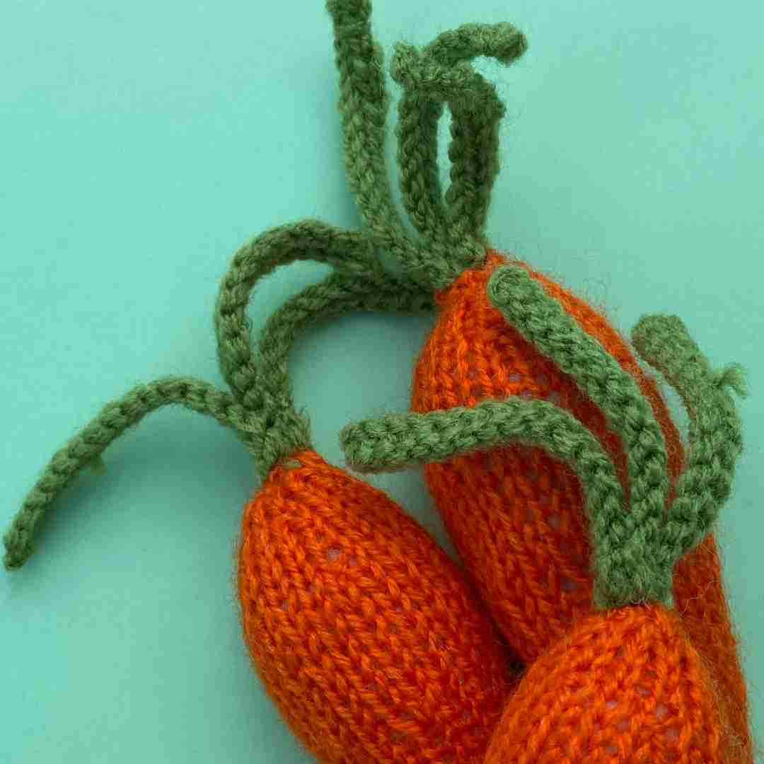 Close up of three knitted carrots made from free knitted carrot pattern, showing green stalks made with I-cord knitting