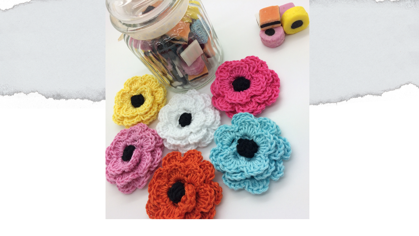 Crochet flower brooch from free flower crochet pattern. Shown in colours of liquorice all sorts with jar of sweets in background