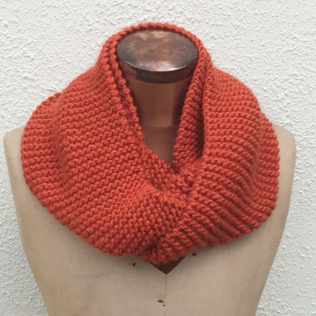 knitted cowl in garter stitch using rust coloured yarn. Wrapped twice around the neck of a sewing dummy. Made from free knitting pattern.