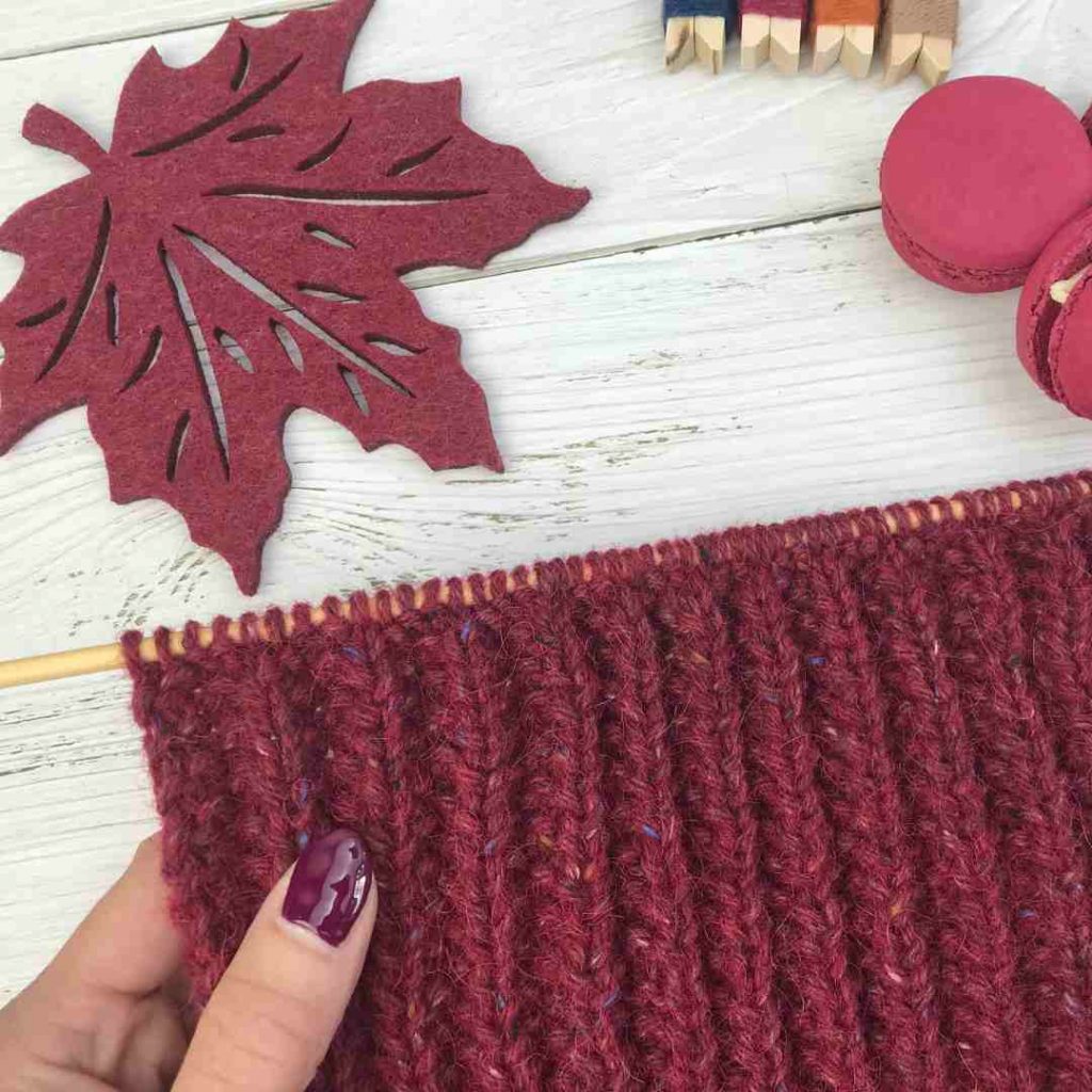 hand holding knitted pumpkin part-made on a knitting needle, in rust-red yarn
