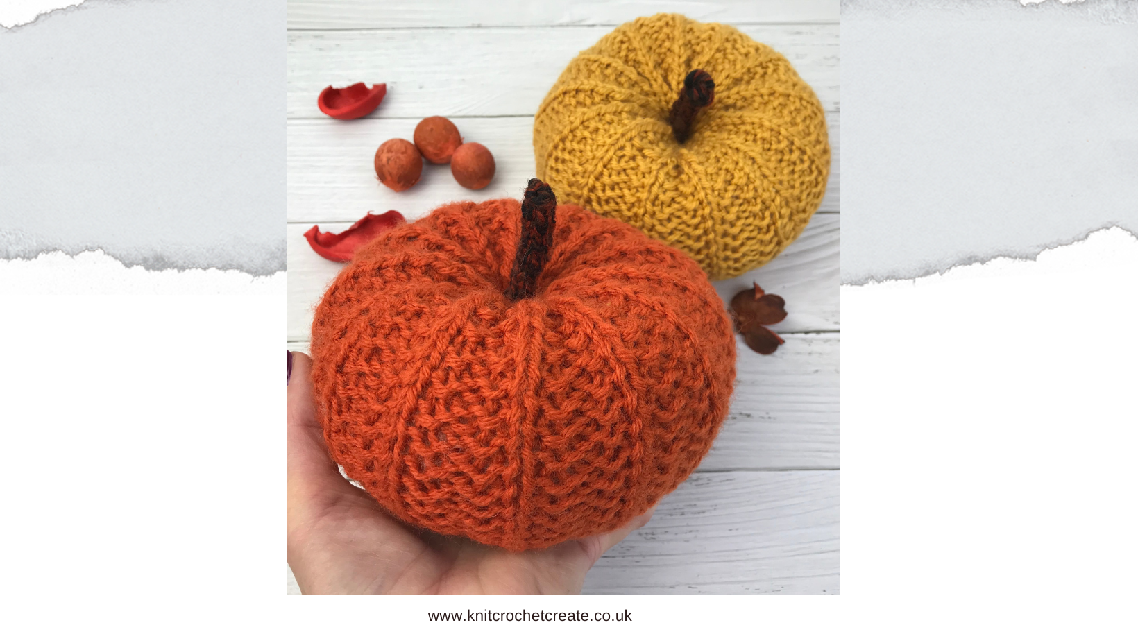 Hand holding a large knitted pumpkin in rust coloured yarn with a mustard knitted pumpkin in the background with scattered nuts and leaves