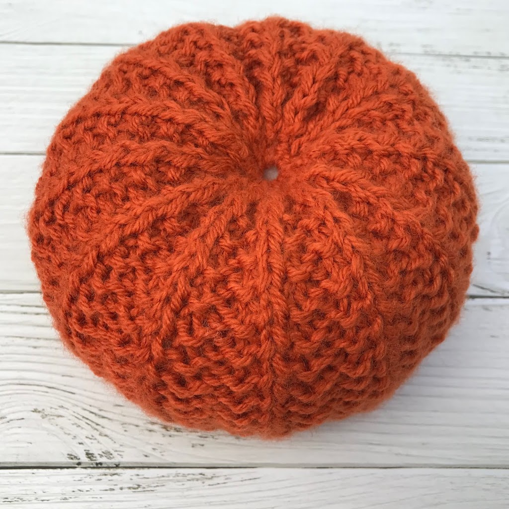 Hand knitted pumpkin in rust coloured yarn with mustard pumpkin in background