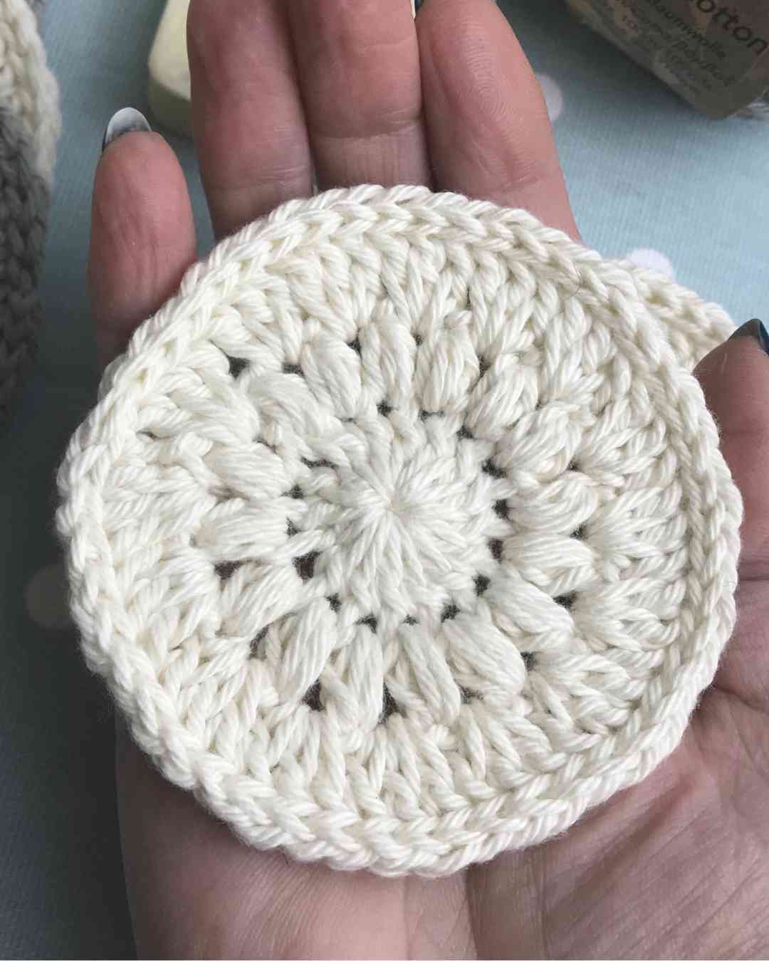 hand holding a round crochet scrubbie in cream yarn