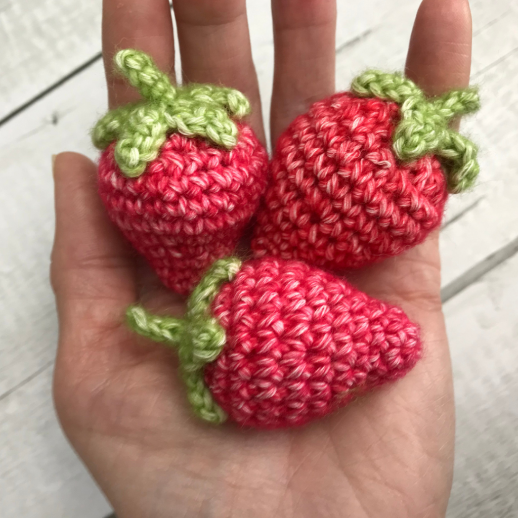 had holding three crochet strawberries made from free crochet pattern