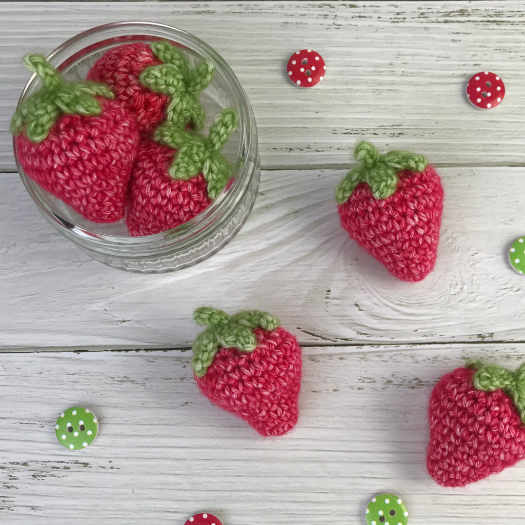 6 crochet strawberries made from free crochet pattern, with 3 in a glass bowl and 3 scattered around.