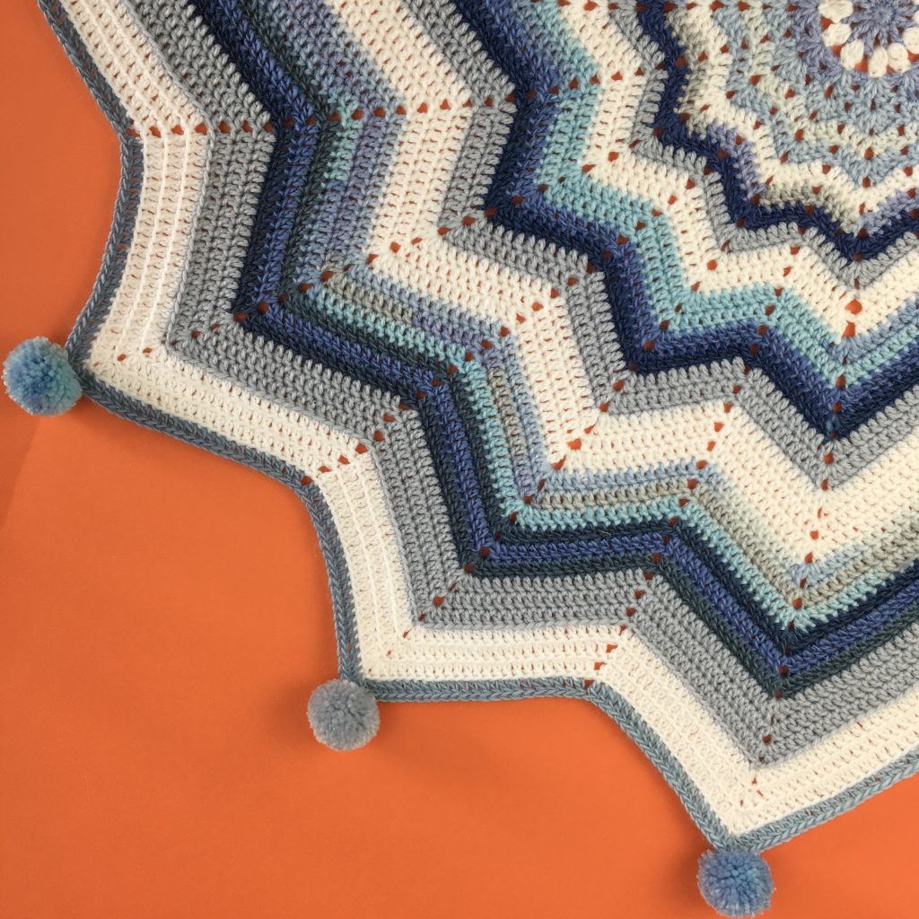 Crochet baby blanket in different shades of blue, with white, in a star shape, created by ripple stitch crochet.