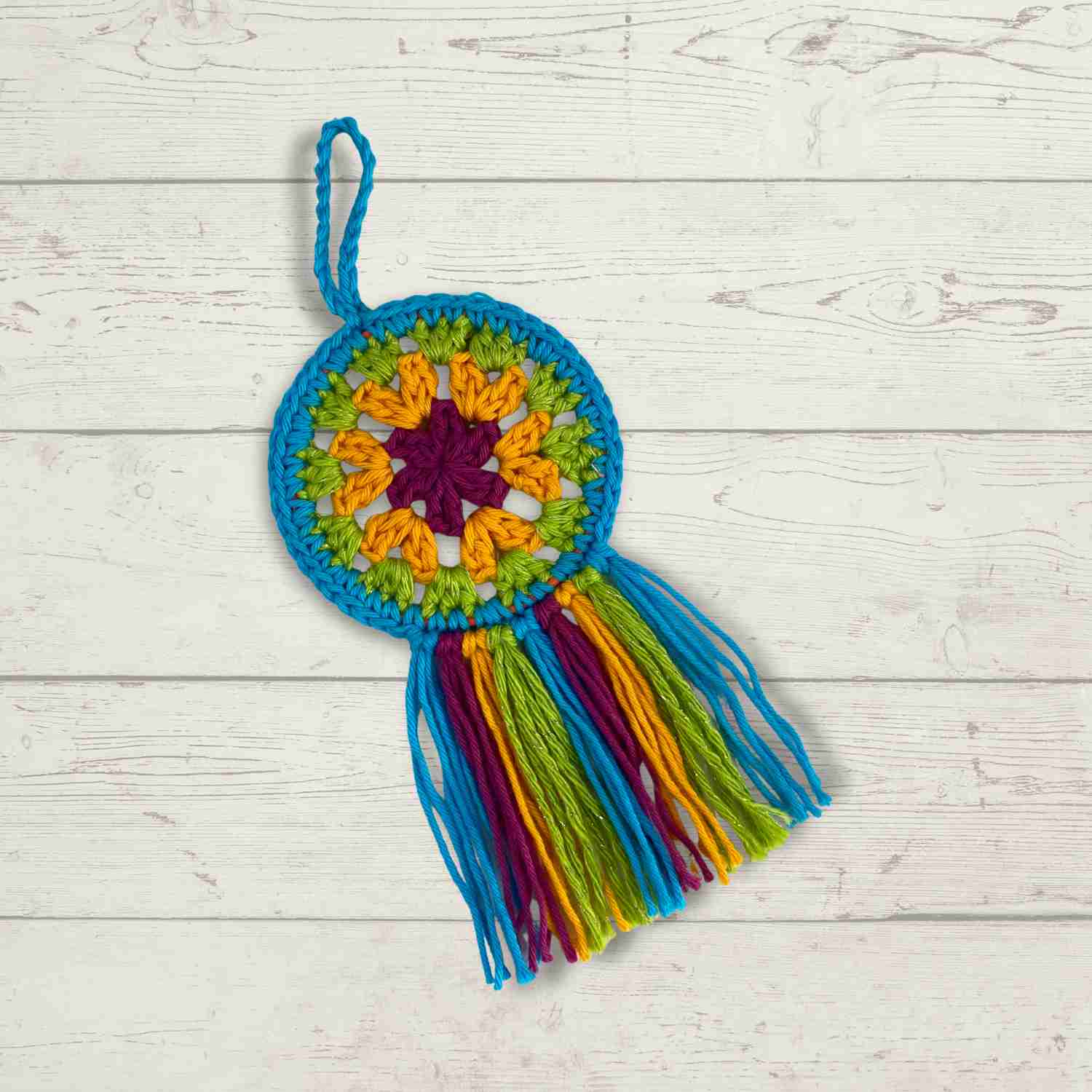 Flat lay of mini mandala crochet hoop, shown against a light grey wooden floor, crocheted in colourful cotton yarn oddments.