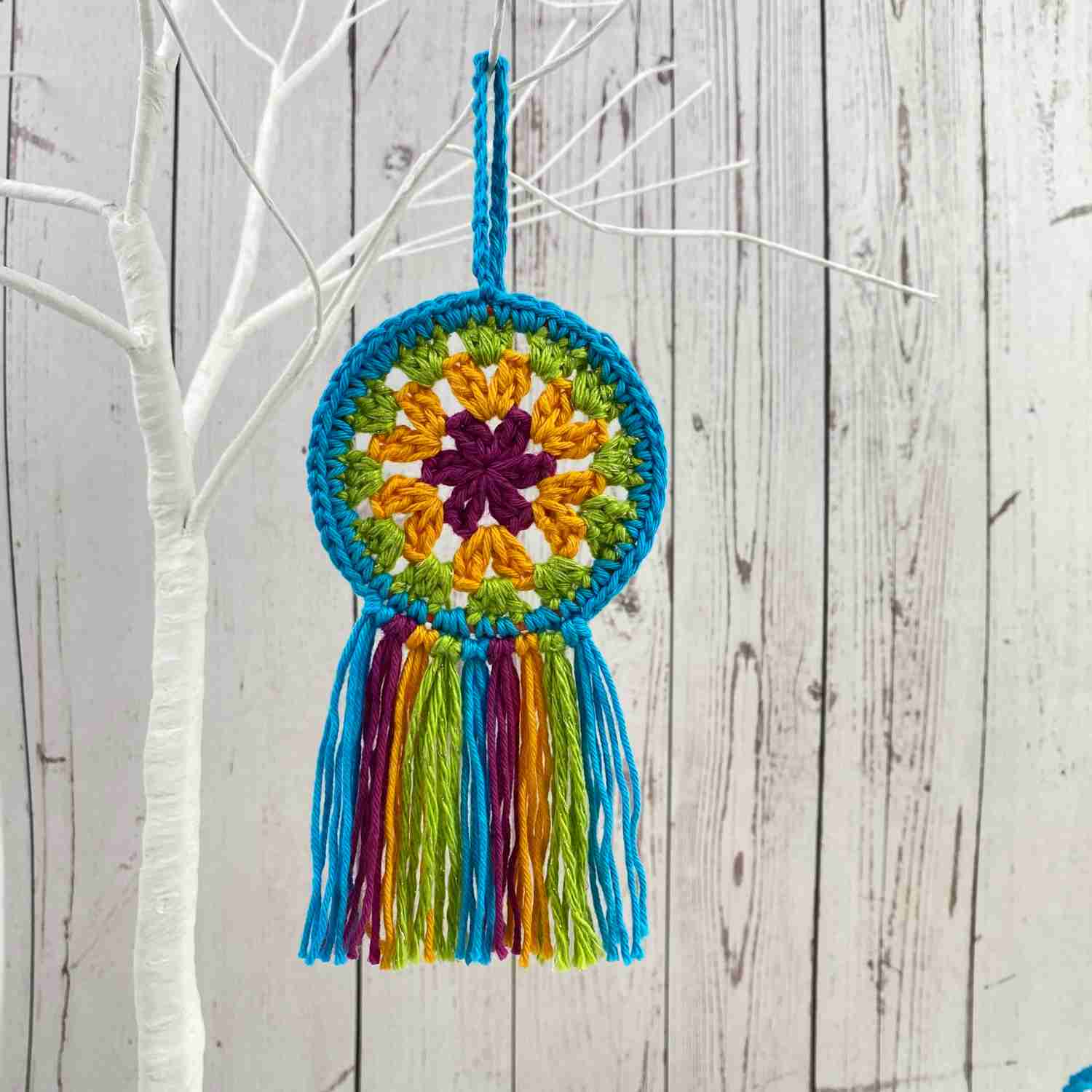 Mini Mandala Crochet Hoop made from free crochet pattern, shown in four colours of cotton yarn, hanging on a white wooden tree.
