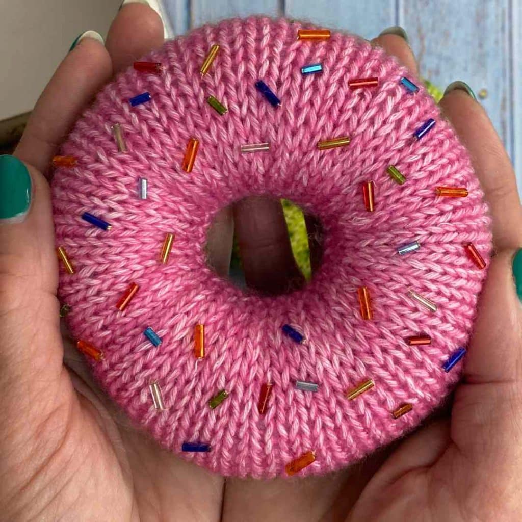 Knitted donut in pink with colourful sprinkles, made from free knitted donut pattern