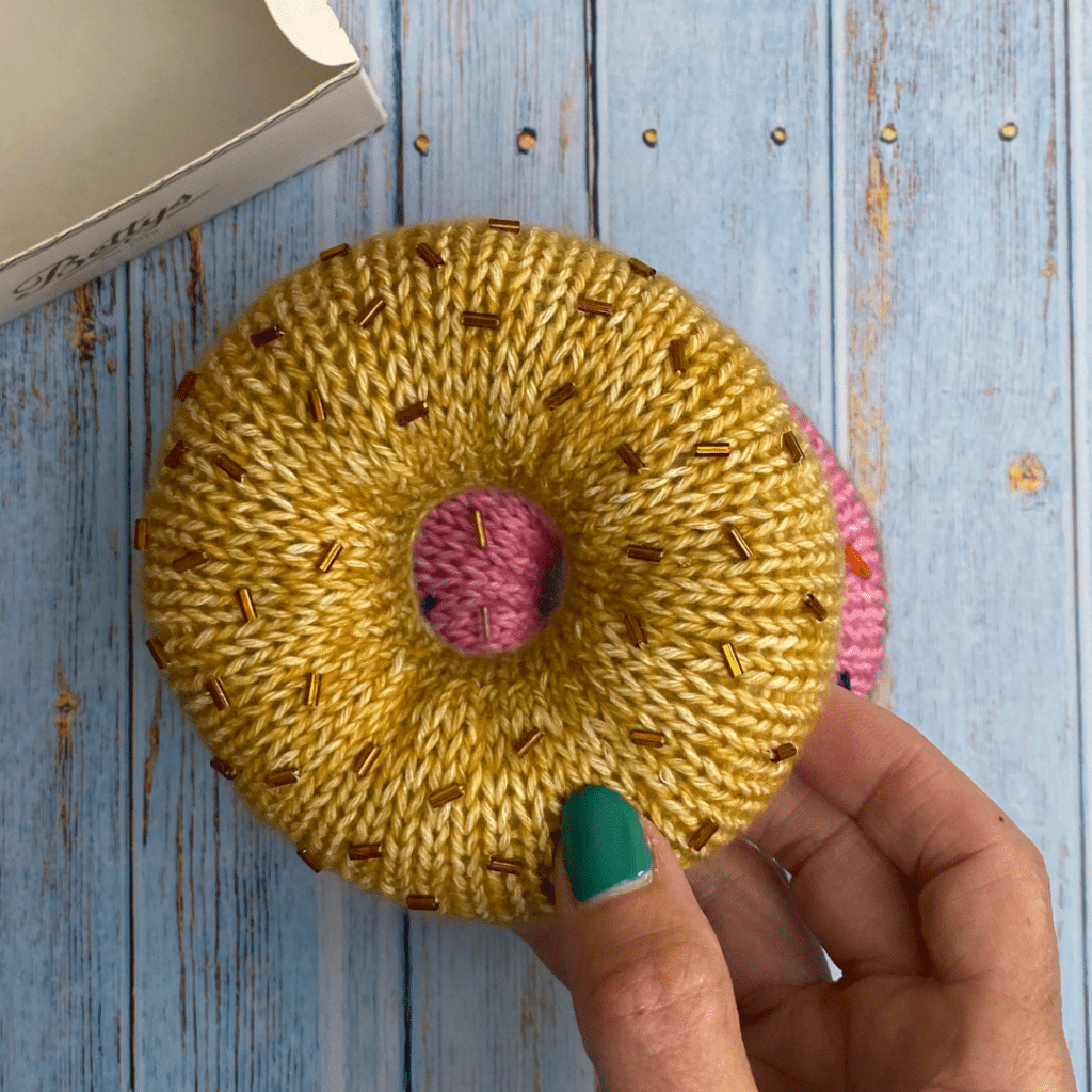 Knitted donut in brown with brown sprinkles, made from free knitted donut pattern