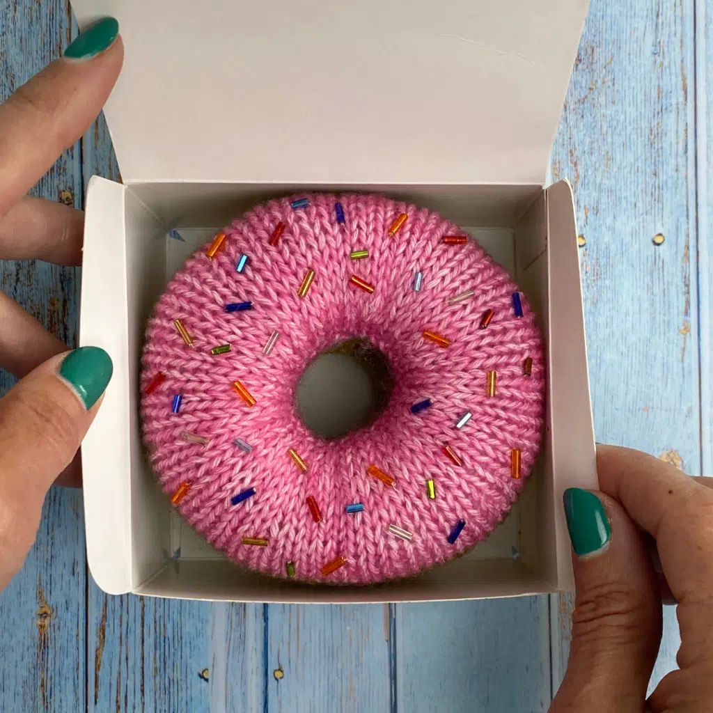 Knitted donut in pink with colourful sprinkles, made from free knitted donut pattern