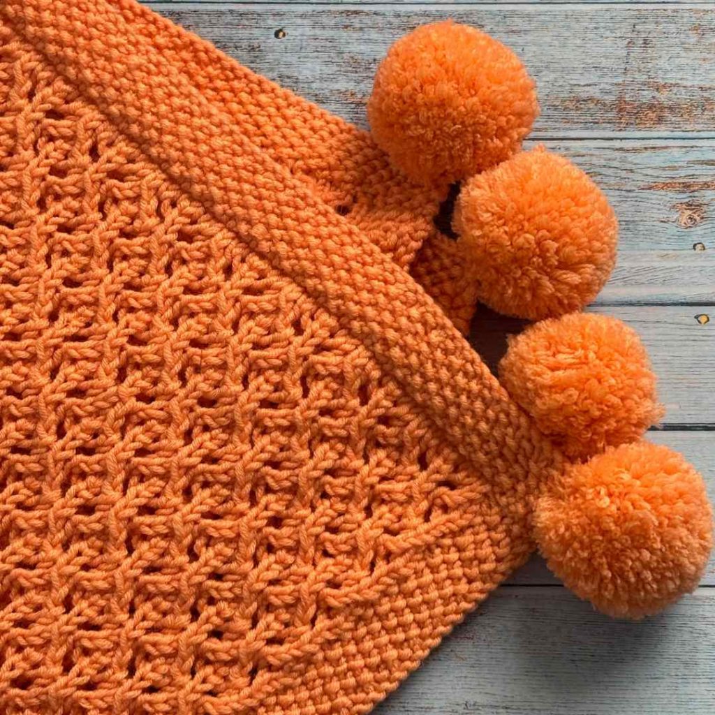 Orange baby blankets made from free baby blanket knitting pattern. Folder to show pompoms.