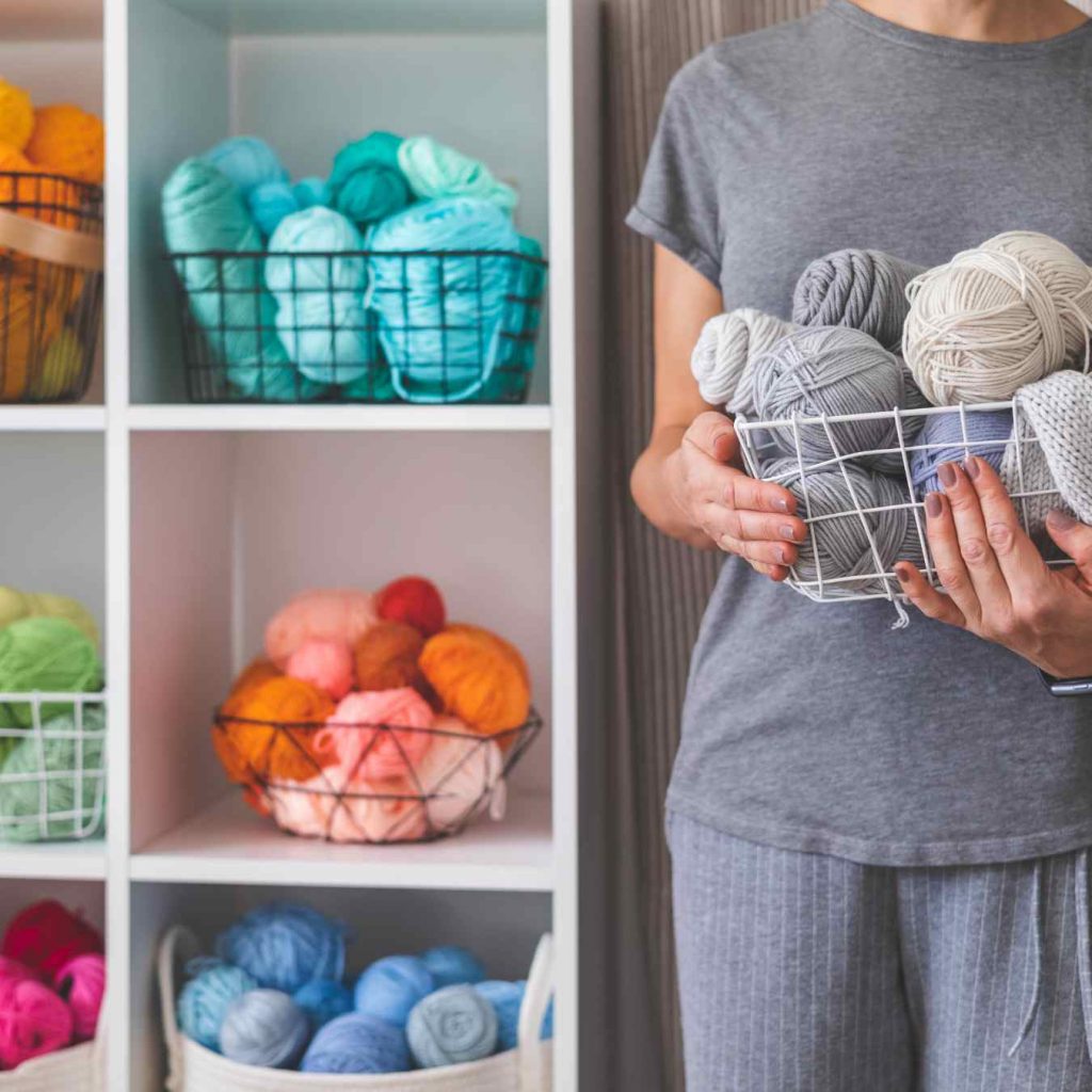 yarn beautifully arranged on shelves and held in a basked by a lady dressed in grey