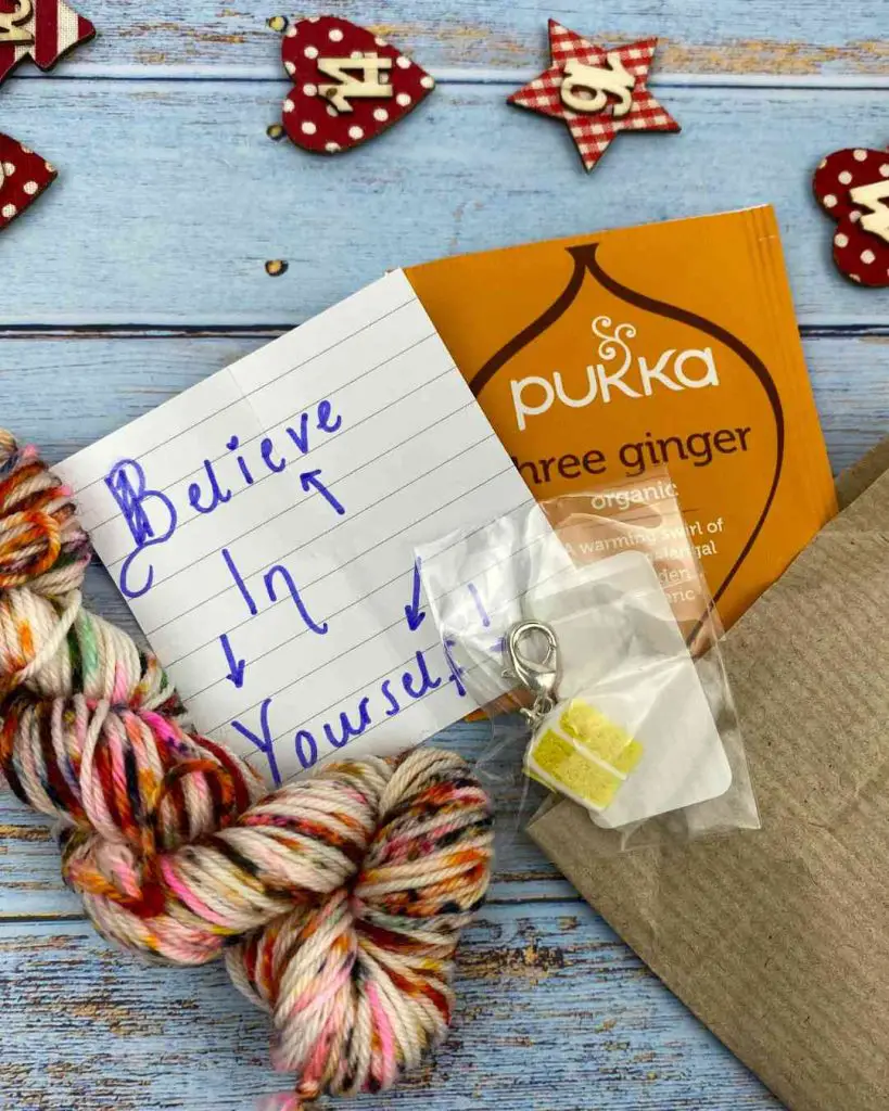 tea bag, yarn mini skein and stitch marker in the shape of cake, showing contents of a yarn advent 