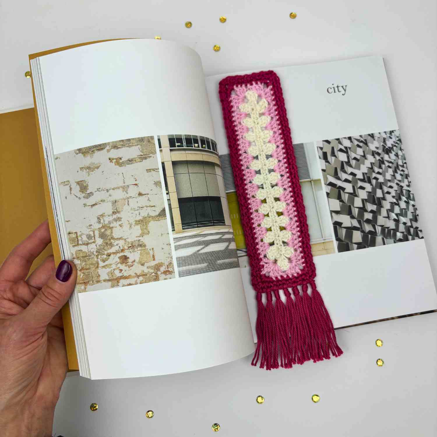 Showing pink version of bookmark in the pages of a book with a hand holding the book open.