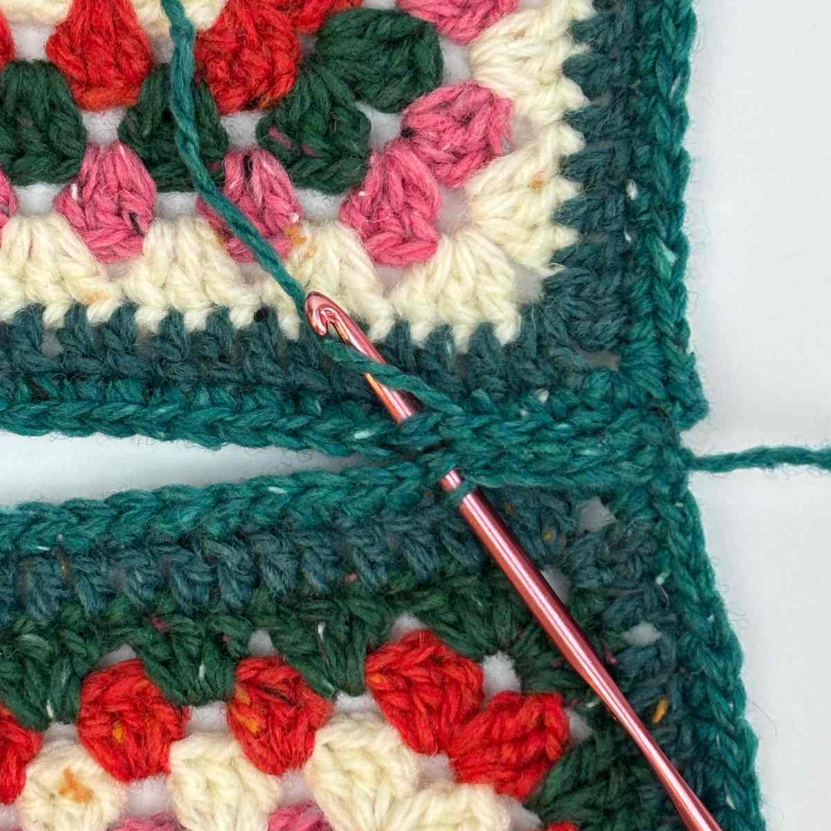 Showing hook inserted under both loops of Granny Squares to join and create crossbody bag shape.