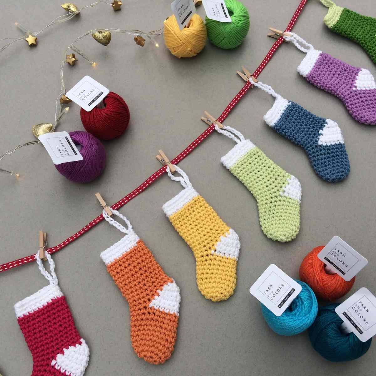 Colourful Mini Crochet Stockings strung onto a thin red ribbon with wooden pegs for a rustic feel.