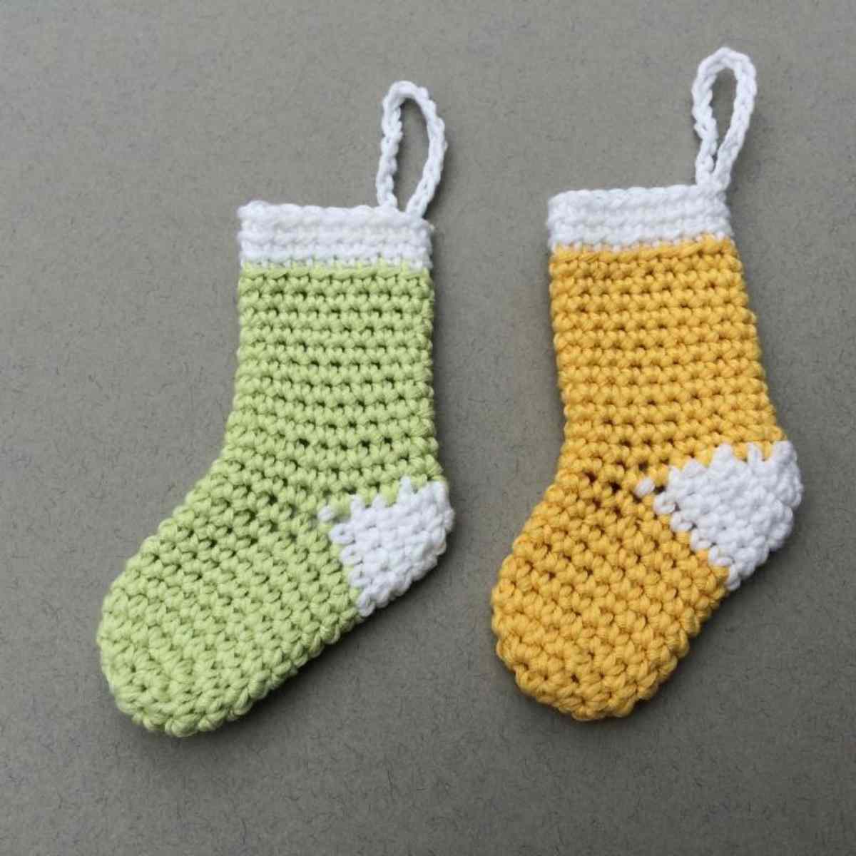 Two mini crochet stockings shown in pale green with White heel and cuff, and yellow with white heel and cuff.