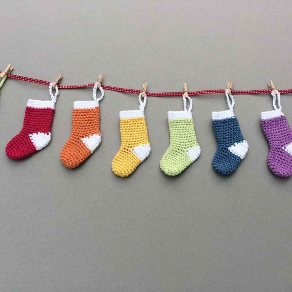 Colourful Mini Crochet Stockings strung onto a thin red ribbon with wooden pegs for a rustic feel.