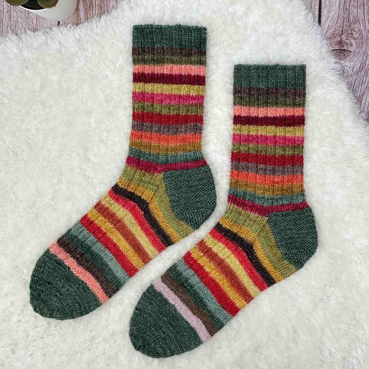 Knitted Stash Yarn Socks shown in self-striping yarn in Greens and Mustards, and reds.