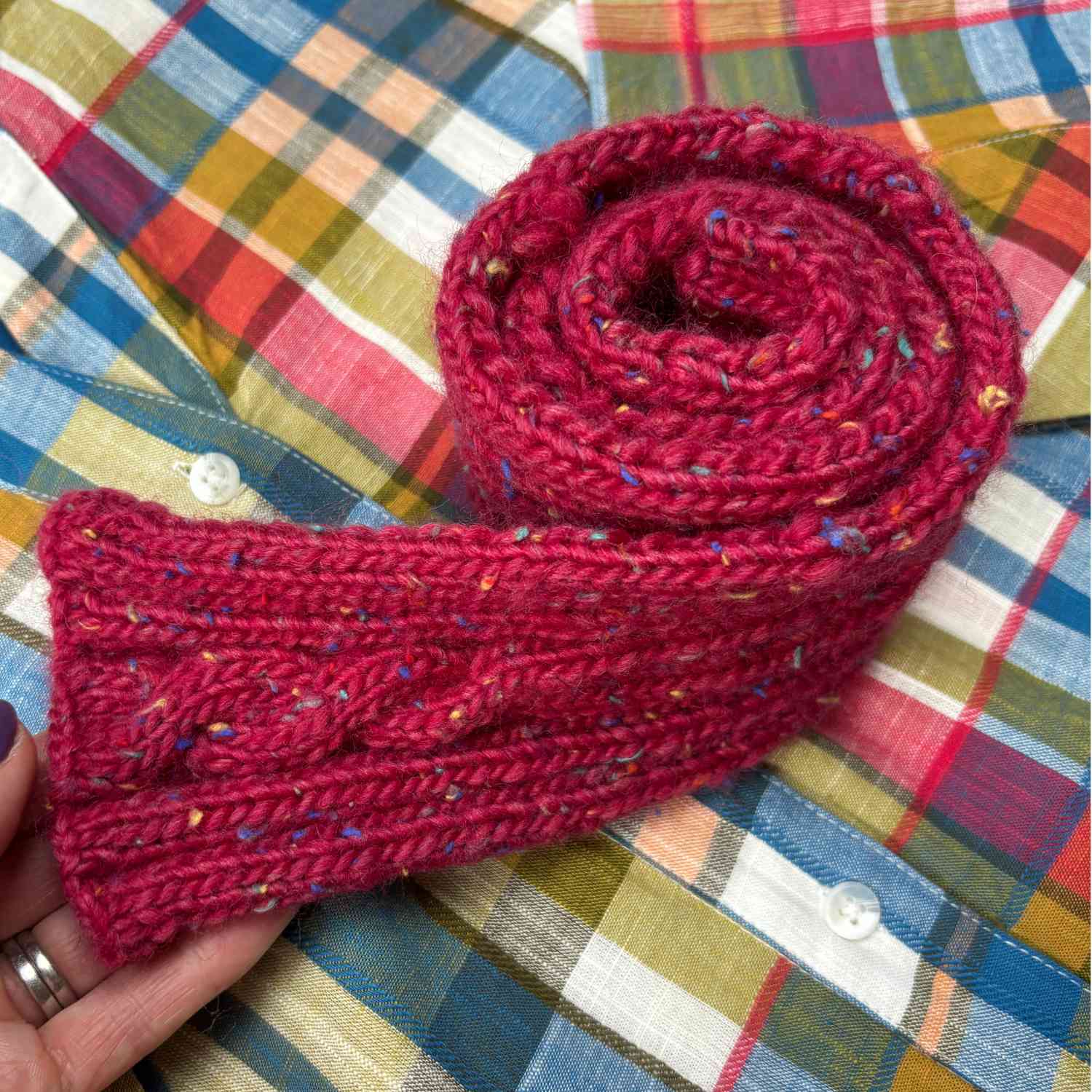 Cable Scarf shown rolled up, on a checked dress background.