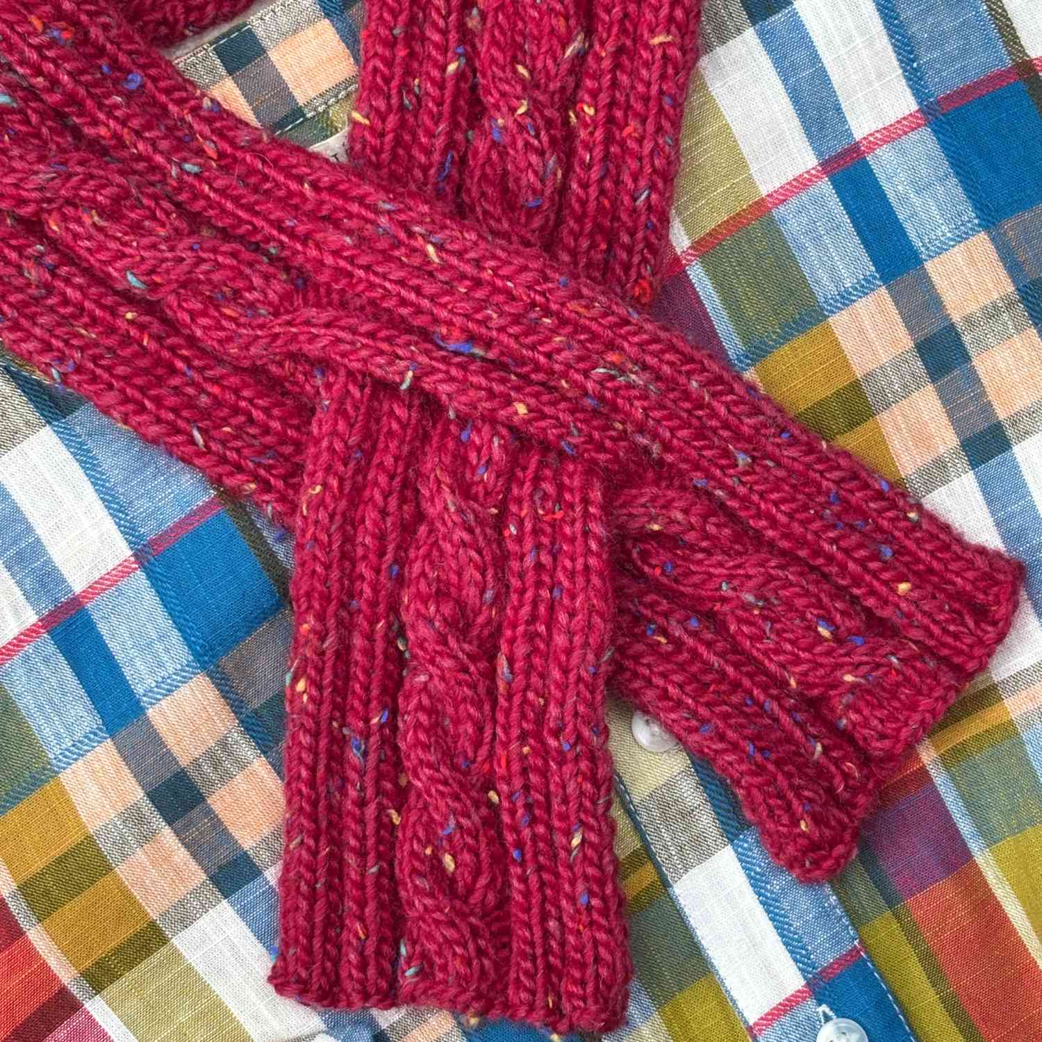 Close up of knitted keyhole scarf shown in tweed yarn in deep red with colourful flecks.