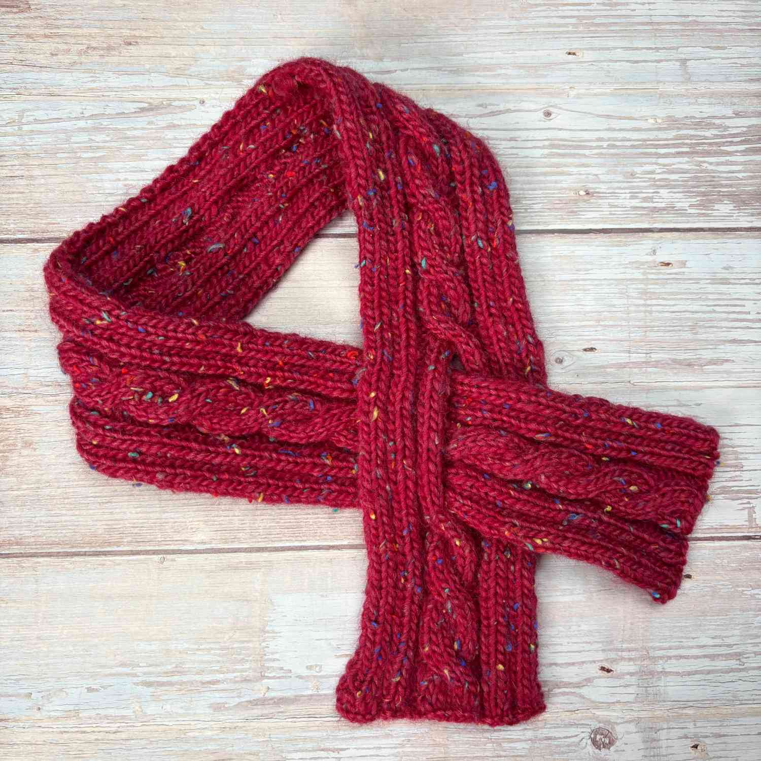 Close up of knitted neck warmer shown in tweed yarn in deep red with colourful flecks.