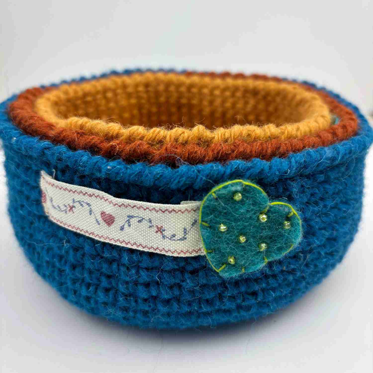 Set of three crochet nesting bowls, made from free crochet bowl pattern, stacked inside each other, in Blue, Rust and Mustard yarn colours.