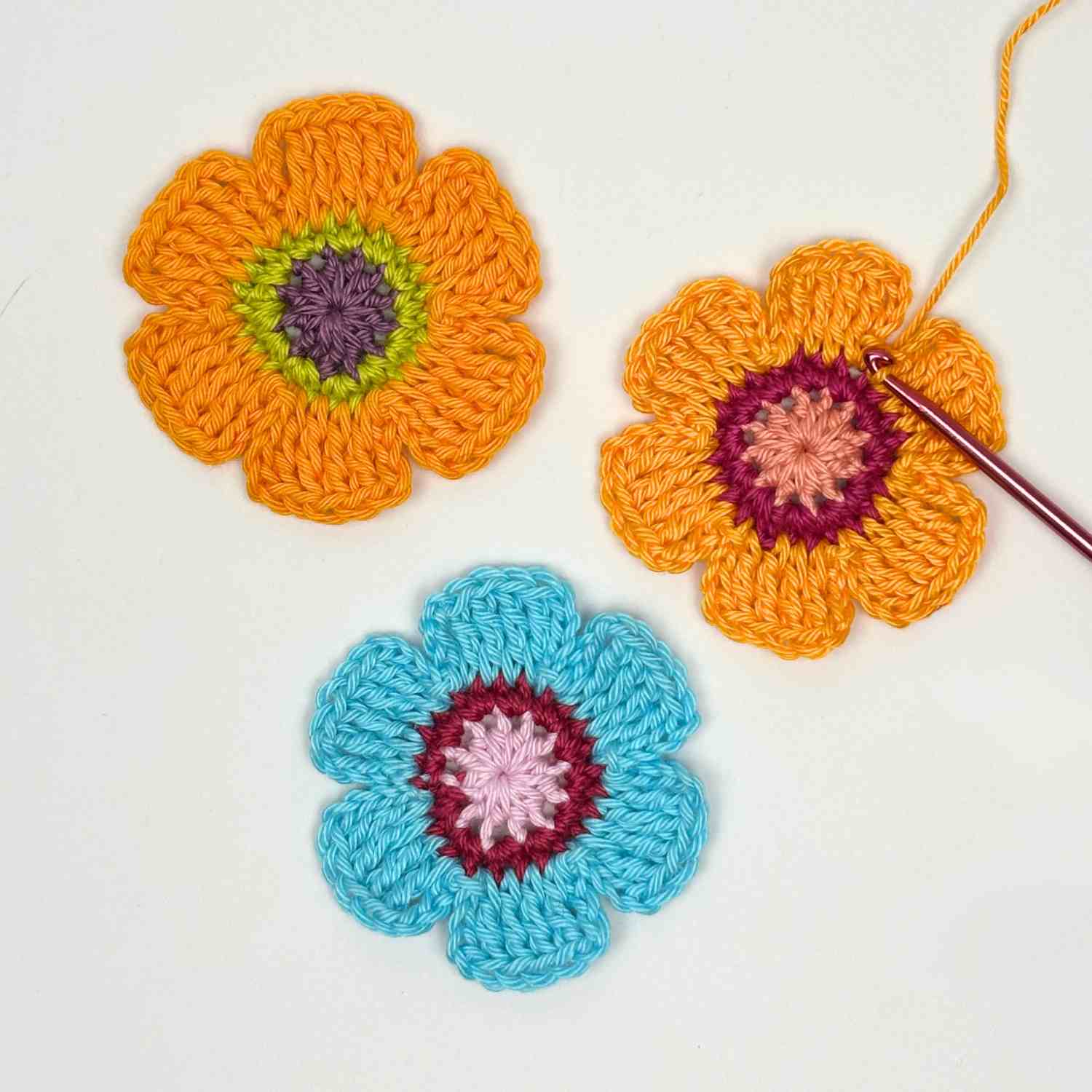 three crochet flowers made from free crochet wreath patter in bright yellow and blue cotton yarn.