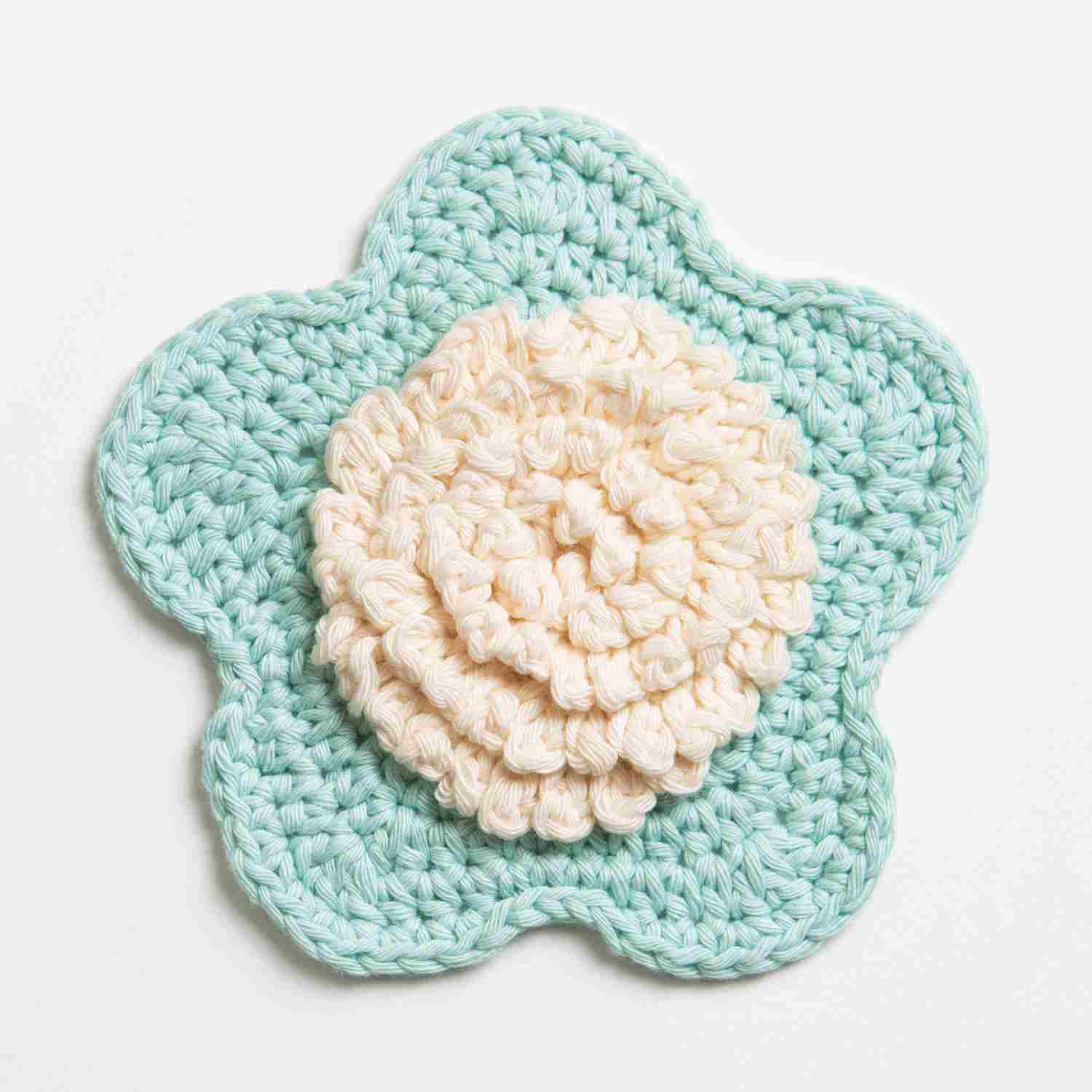 Crochet flower washcloth with a textured centre in cream and pale blue petals.