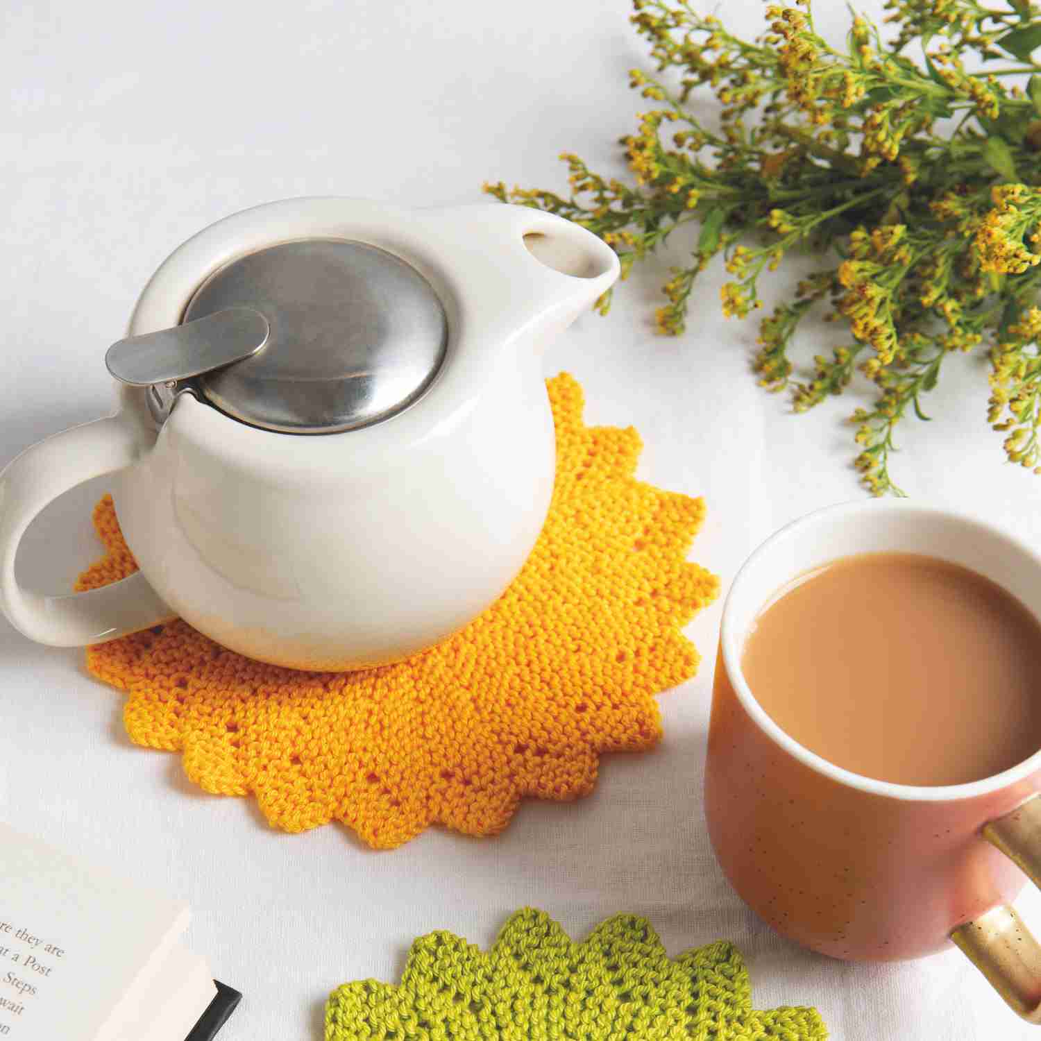 Knitted circle dishcloth pattern made in bright sunflower yellow yarn and pea green yarn. Shown with a cup of tea and tea pot.