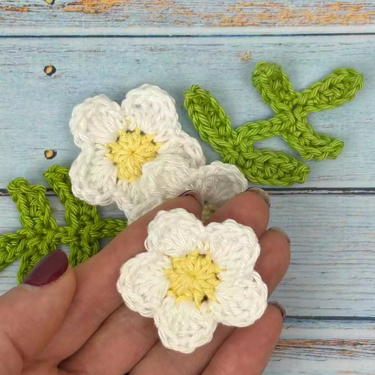 2 mini crochet flower motifs made from free crochet pattern, hand is holding one crochet flower.