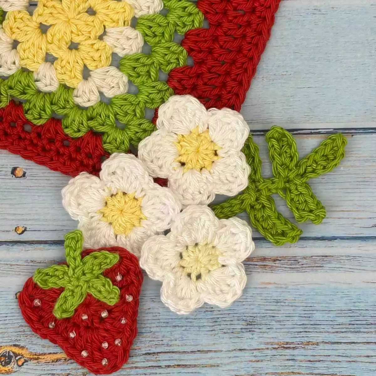 Flatlay of crochet flowers and leaf stem, made from free mini flower crochet pattern, shown with a crochet strawberry.