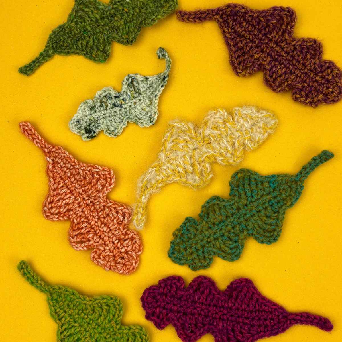 Crochet oak leaves in autumnal fall colours, scattered across a yellow background.
