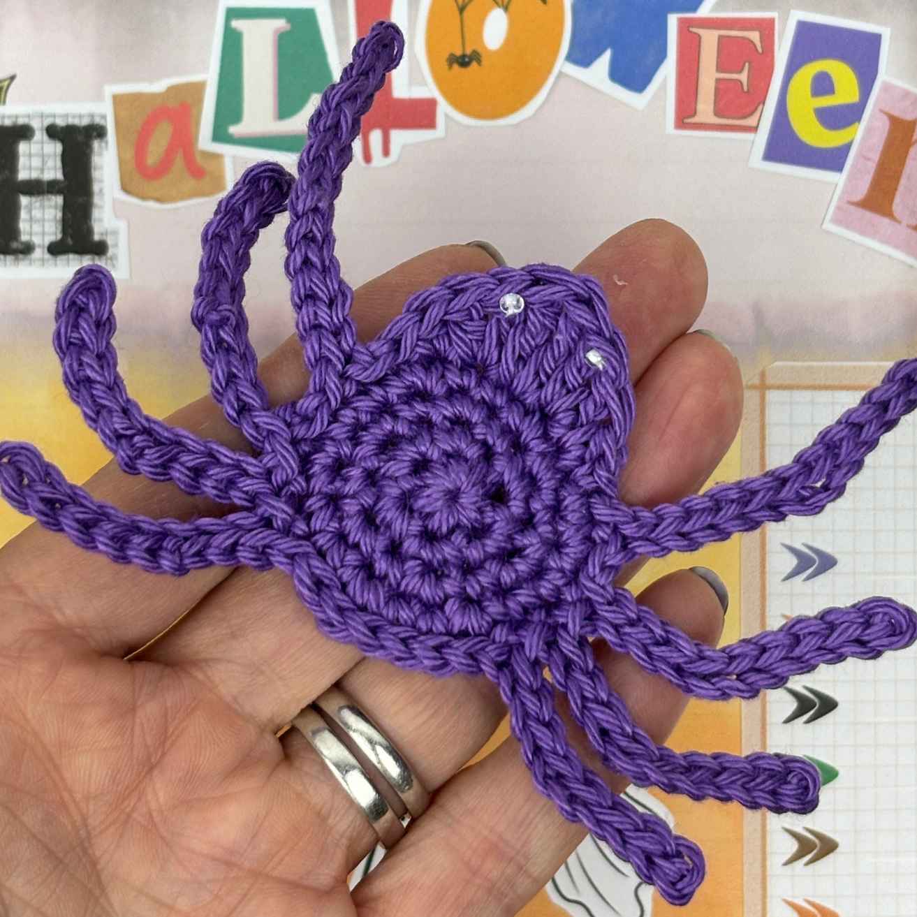 Crochet Spider Appliqué Motif made from free crochet pattern, shown in Purple cotton yarn on palm of hand.